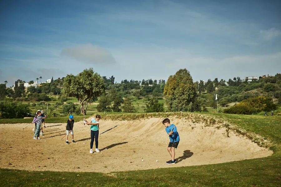 Junior golfers practising bunker play with a PG coach